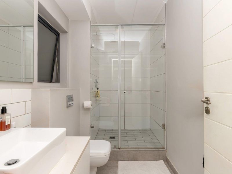 A modern, clean bathroom featuring a glass-enclosed shower, wall-mounted toilet, and a contemporary vessel sink with a large mirror.