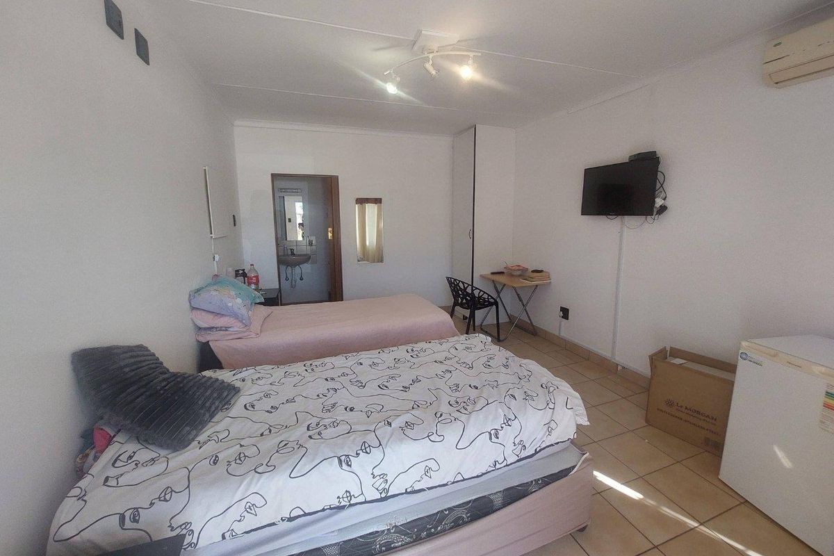 A functional bedroom featuring tiled flooring, a wall-mounted air conditioning unit, and an en-suite bathroom access.