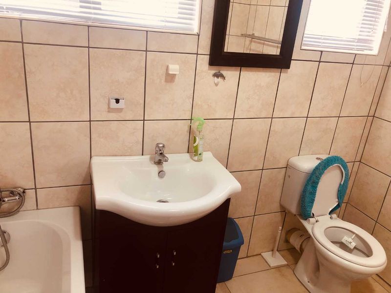 A functional bathroom featuring a vanity cabinet with basin, a standard toilet, and a bathtub, finished with neutral wall and floor tiling.