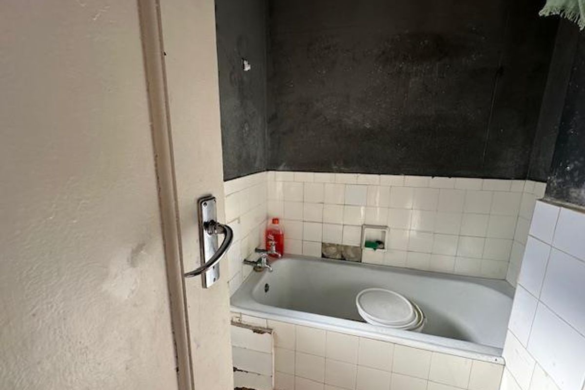 A bathroom in need of renovation, featuring a bathtub with missing wall tiles and damaged paneling, requiring significant cosmetic and structural repairs.