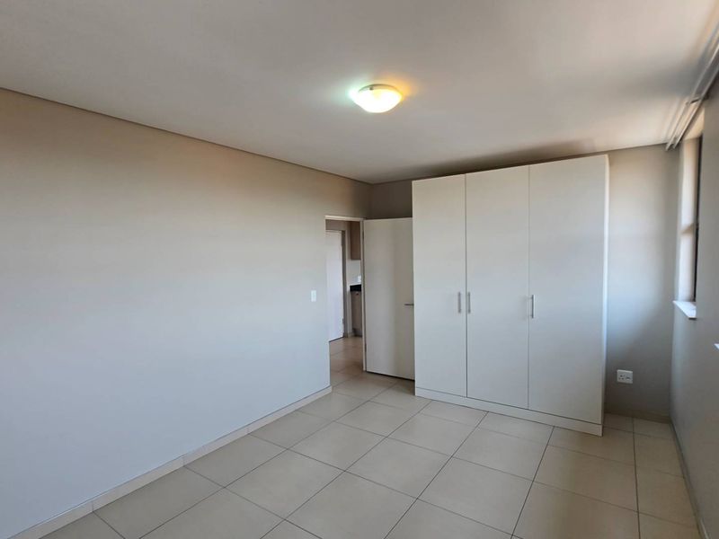 A bright and spacious bedroom featuring neutral tiled flooring and a large built-in wardrobe, offering a clean and versatile living space.