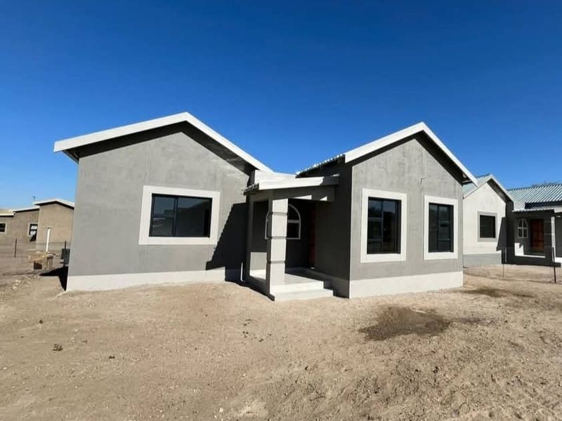 A modern, newly constructed single-story house featuring a grey plastered facade, dark aluminium window frames, and a covered entrance porch.
