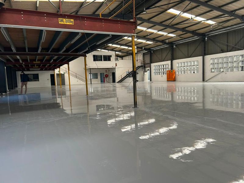 Spacious industrial warehouse featuring a polished epoxy floor, steel mezzanine level, high-clearance roof trusses, and natural light through skylights and glass block windows.