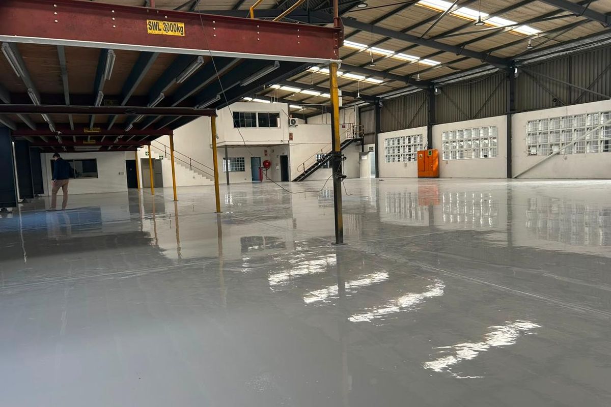 Spacious industrial warehouse featuring a polished epoxy floor, steel mezzanine level, high-clearance roof trusses, and natural light through skylights and glass block windows.