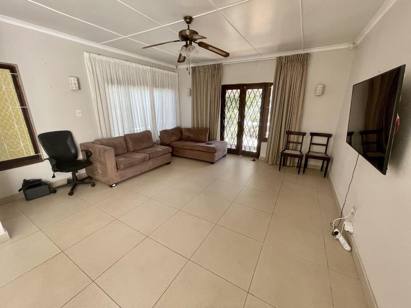 A spacious living room featuring neutral tiled flooring, a ceiling fan, and direct access to the outdoors through secure french doors.