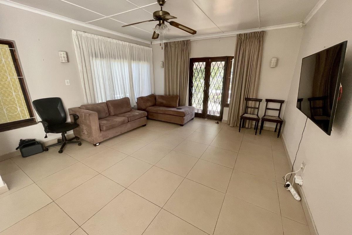 A spacious living room featuring neutral tiled flooring, a ceiling fan, and direct access to the outdoors through secure french doors.