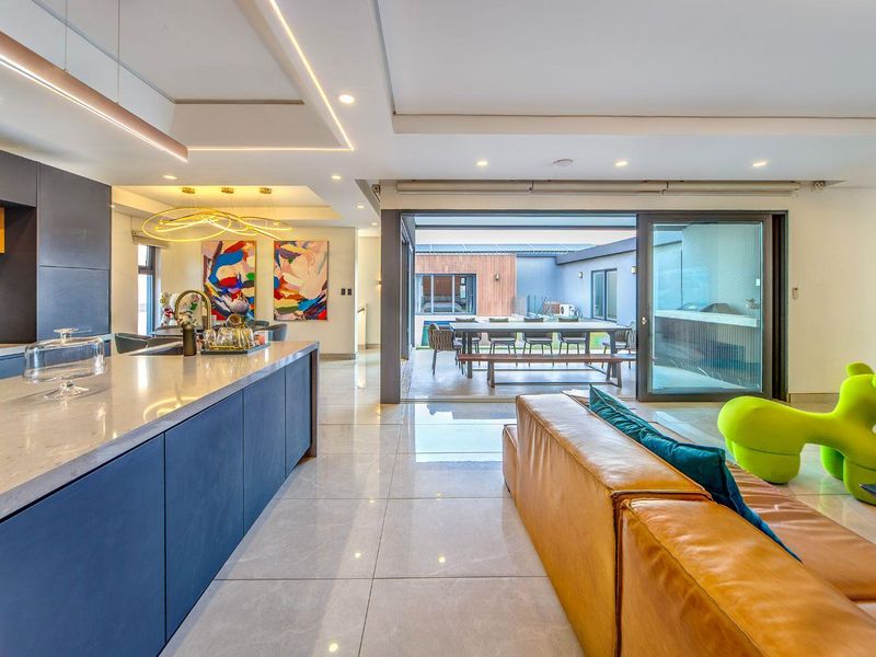 Modern open-plan living area featuring a sleek kitchen with stone island, seamless transition to an outdoor patio through large sliding glass doors.