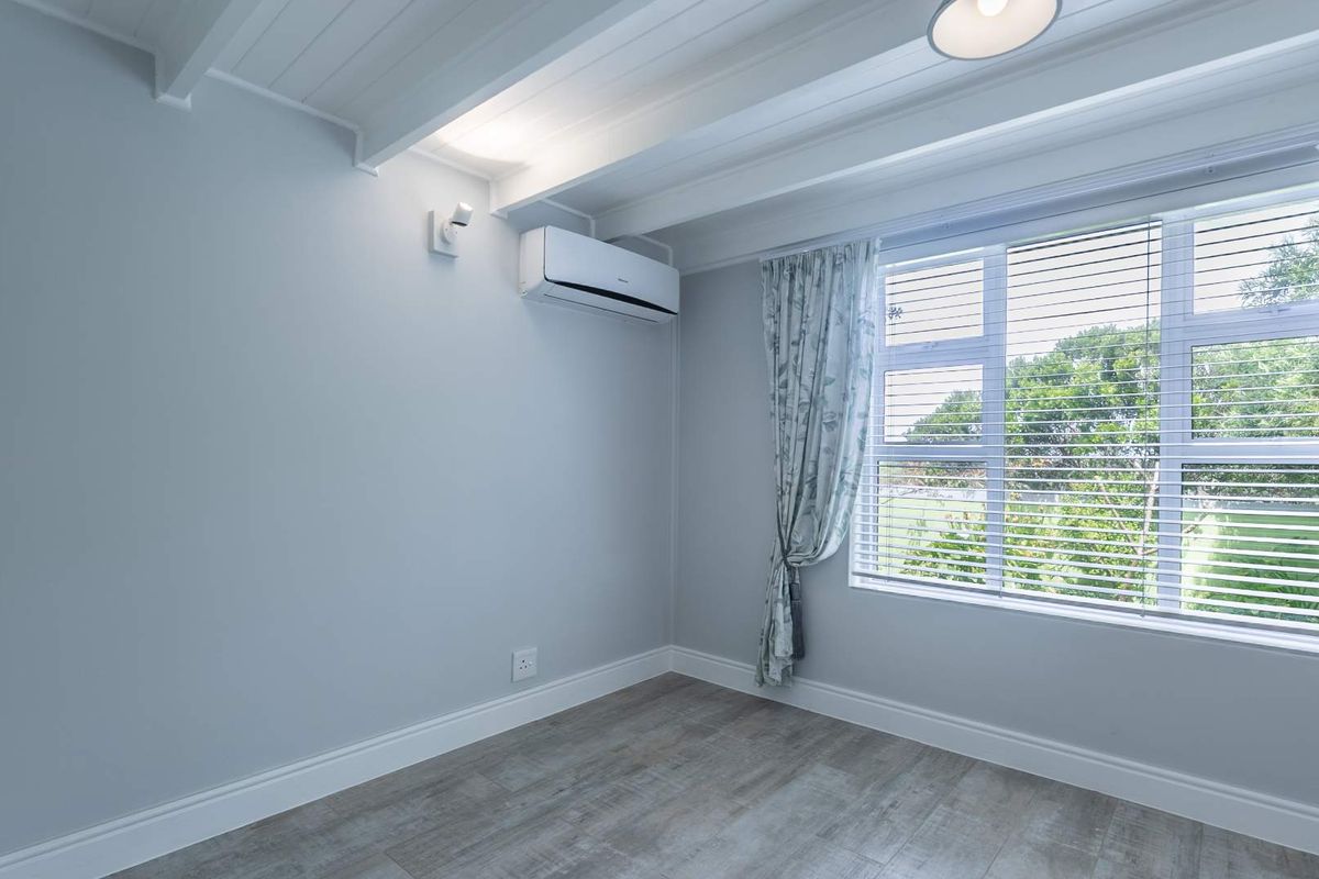A bright, empty bedroom featuring exposed beam ceilings, modern laminate flooring, and a wall-mounted split-system air conditioner.