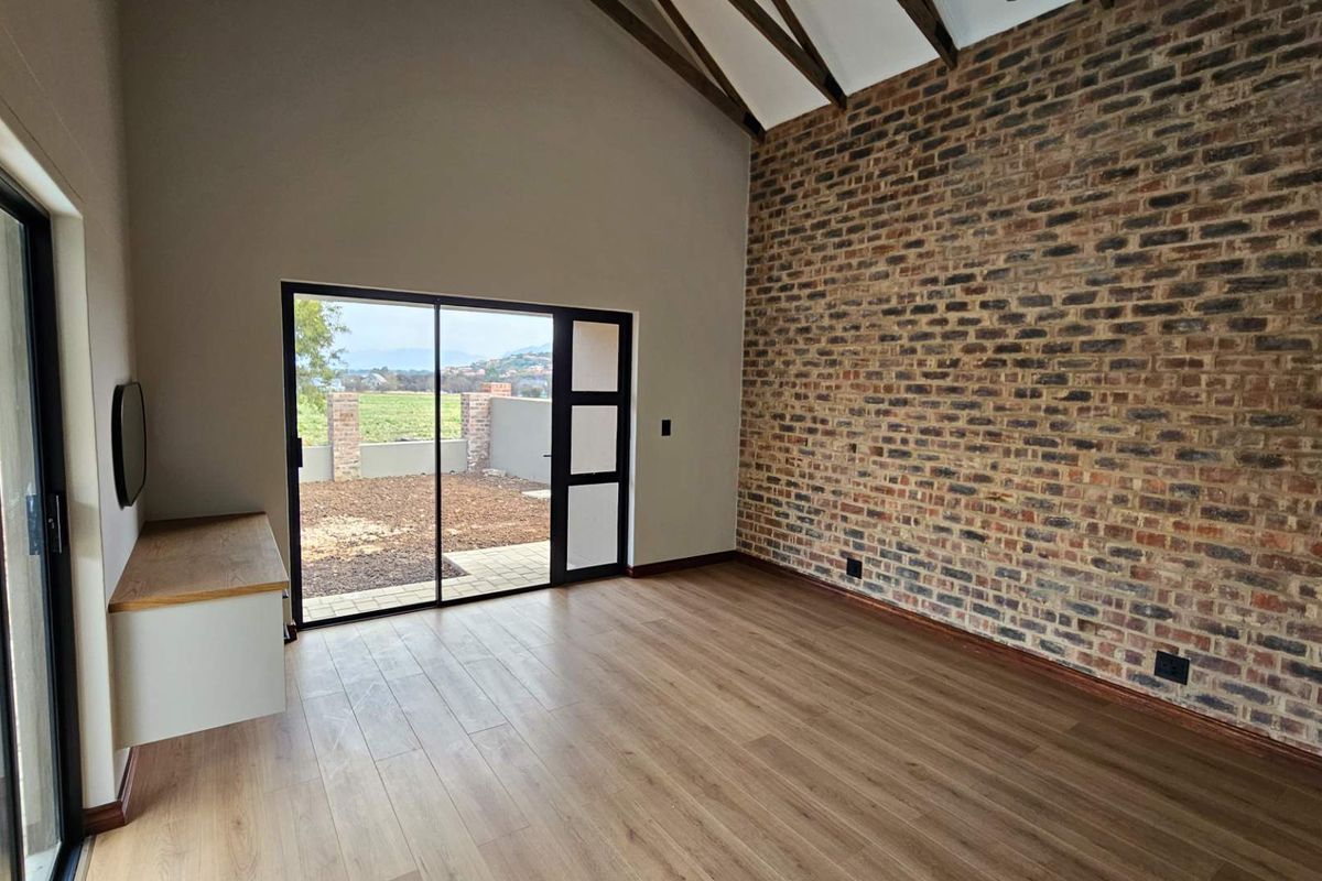 Spacious living area featuring a striking exposed brick feature wall, vaulted ceilings with exposed beams, wood-look flooring, and large sliding doors leading to the garden.