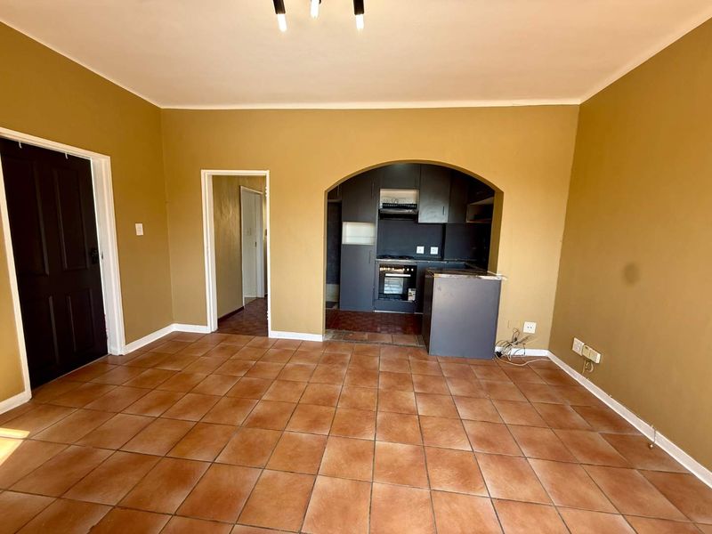 An empty open-plan living area featuring tiled flooring, an arched entryway to the kitchen, and built-in kitchen cabinetry with an integrated oven.