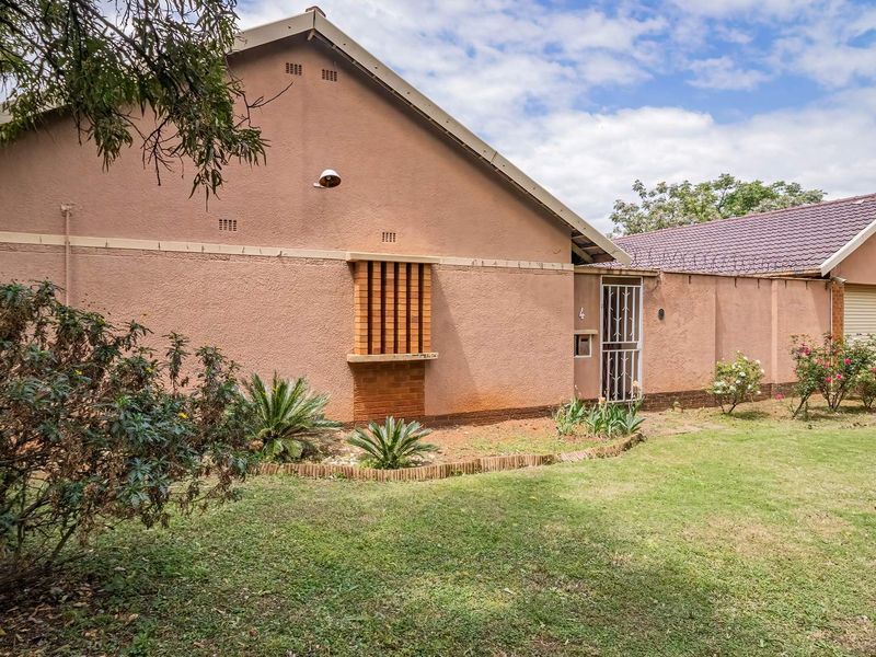 Front exterior view of the house featuring a tiled roof, security gate, and attached garage with a surrounding garden area.