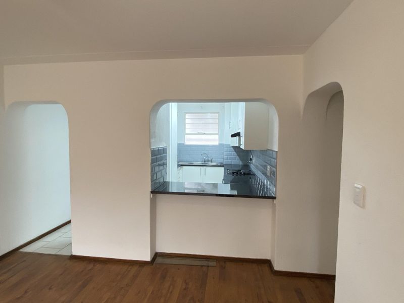 An open-plan living area featuring hardwood flooring, arched doorways, and a functional kitchen pass-through with granite countertops and subway tile backsplash.
