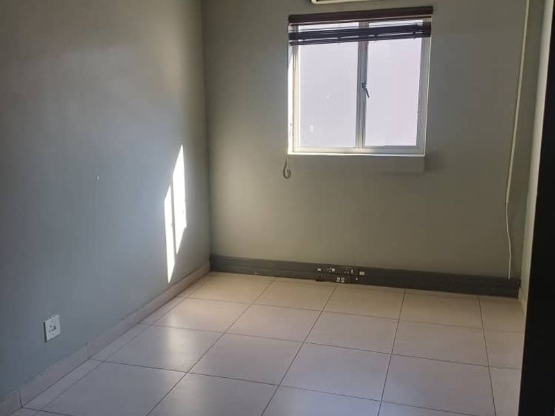 A vacant office space featuring tiled flooring, a suspended ceiling with recessed lighting, and a wall-mounted air conditioning unit.