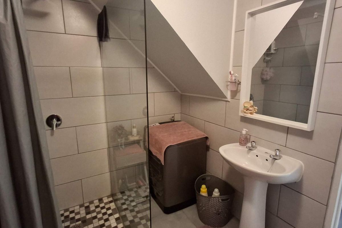 A functional bathroom featuring a pedestal basin, a glass-enclosed shower with tiled walls, and a wall-mounted mirror.