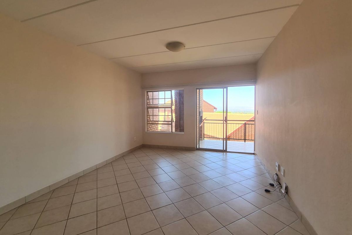 An empty, sunlit living area featuring neutral tiled flooring and a sliding glass door providing access to an outdoor balcony.