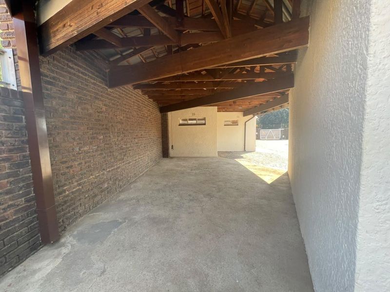 A spacious, open-plan garage area featuring exposed timber roof trusses, a combination of facebrick and textured plaster walls, and concrete flooring.