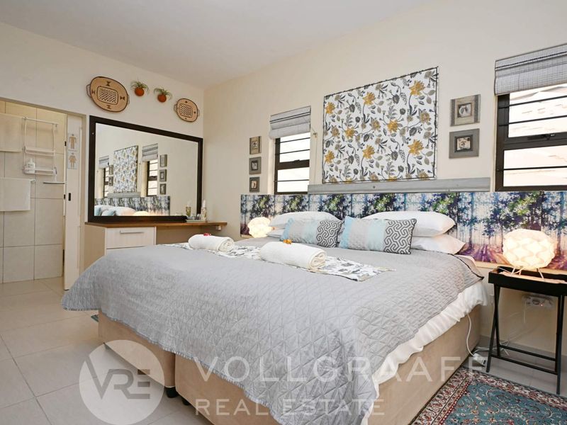 A well-maintained bedroom featuring tiled flooring, built-in vanity, and aluminium window frames with roman blinds, offering a comfortable and functional living space.