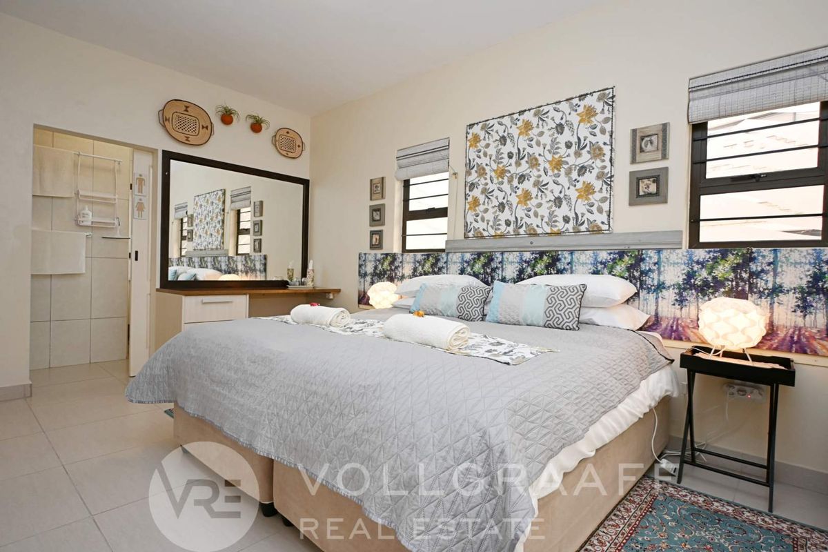 A well-maintained bedroom featuring tiled flooring, built-in vanity, and aluminium window frames with roman blinds, offering a comfortable and functional living space.