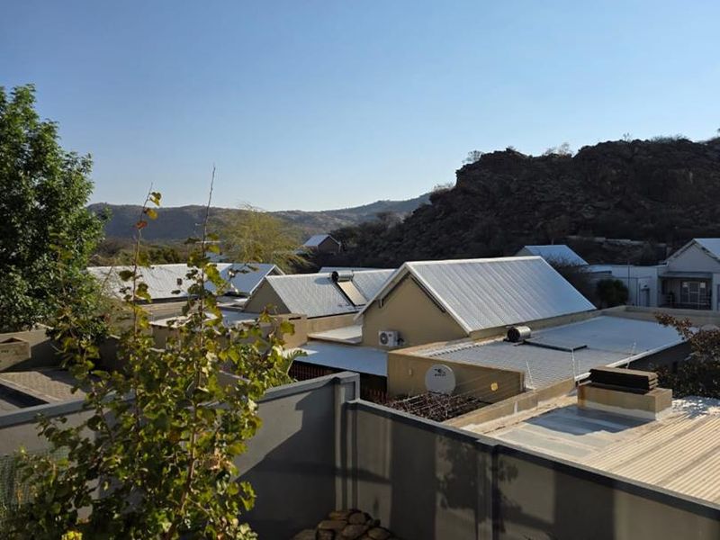 Elevated view overlooking neighbouring residential rooftops and surrounding rocky landscape under a clear blue sky.