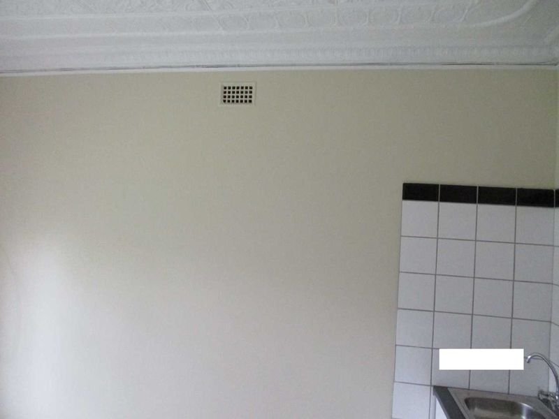 A view of a kitchen wall featuring a tiled splashback, stainless steel sink, and decorative ceiling cornice.