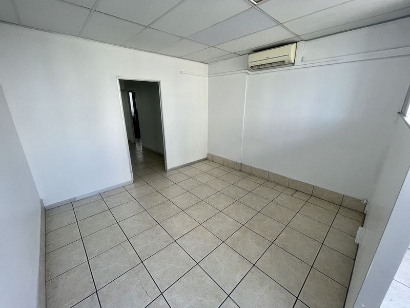 A clean, empty office space featuring ceramic floor tiles, a suspended ceiling, and a wall-mounted split-system air conditioning unit.