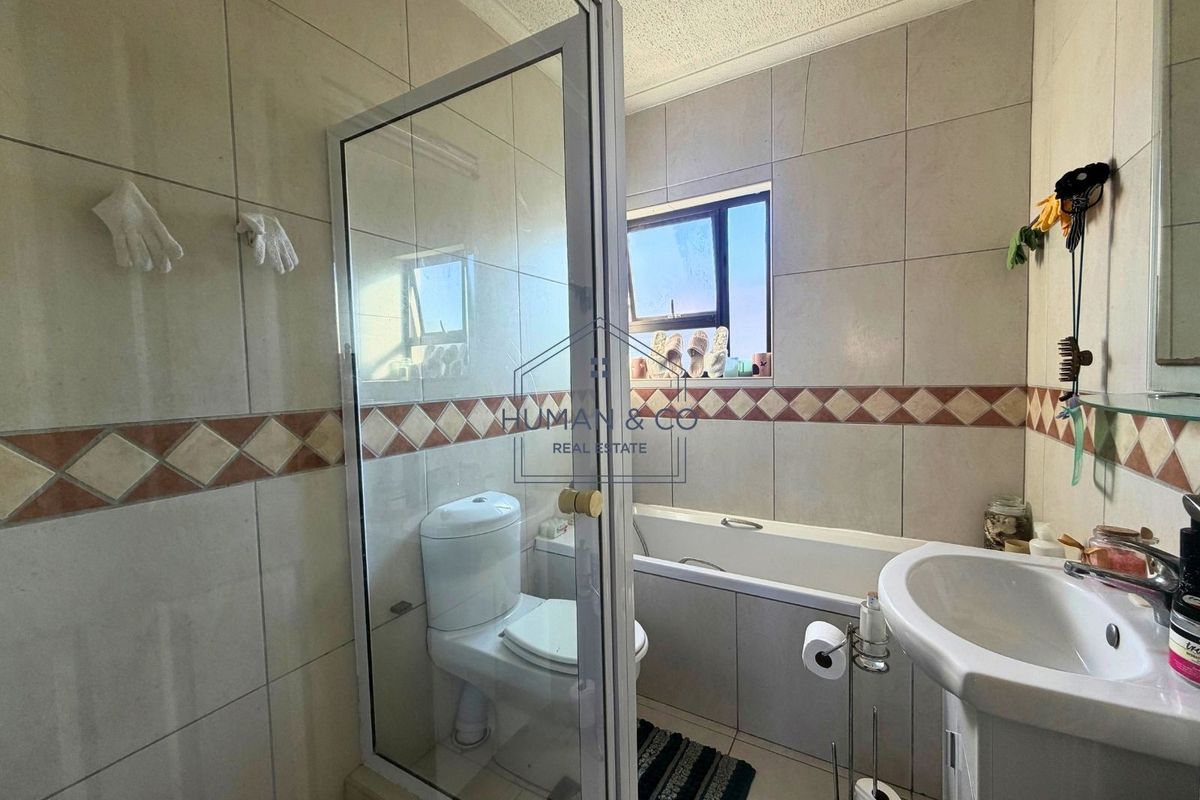 A functional bathroom featuring a shower enclosure, bathtub, pedestal basin, and toilet, finished with neutral wall and floor tiling.