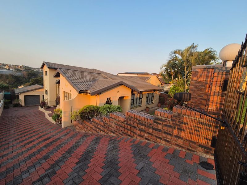Front elevation of a residential house featuring a paved driveway, brick boundary wall, and a tiled roof structure.