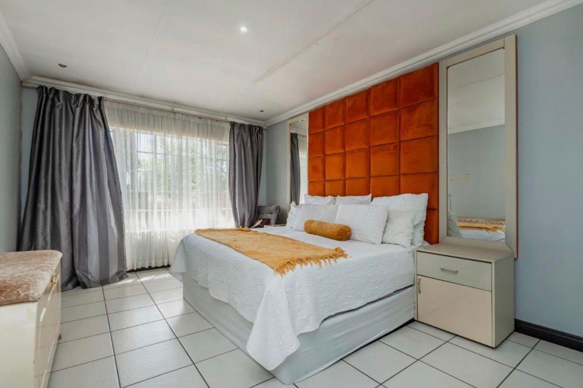A well-lit bedroom featuring tiled flooring, a large window with curtains, and a built-in headboard with integrated mirrors.