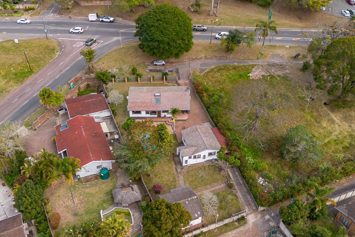 Aerial view of the property showing multiple structures, a swimming pool, lapa, and surrounding garden area with paved driveway access.