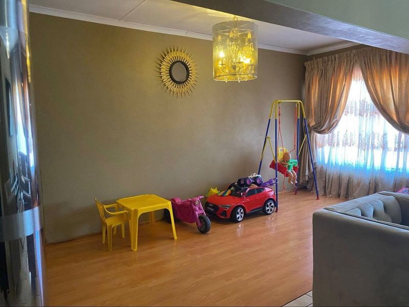 A living room area featuring laminate flooring, neutral wall tones, and a central ceiling light fixture, currently utilized as a play space.