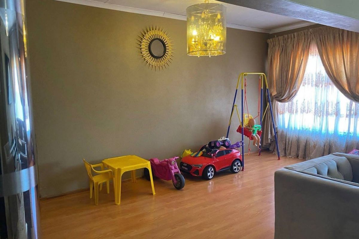 A living room area featuring laminate flooring, neutral wall tones, and a central ceiling light fixture, currently utilized as a play space.