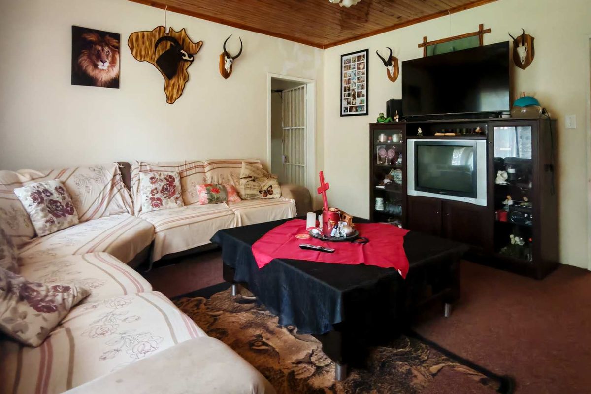 A living room featuring a timber-clad ceiling, carpeted flooring, and access to an adjacent room, providing a functional space for relaxation.
