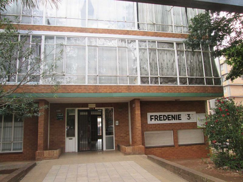 Front entrance view of the Fredenie apartment building, featuring a brick facade, large glass window panels, and a tiled walkway.