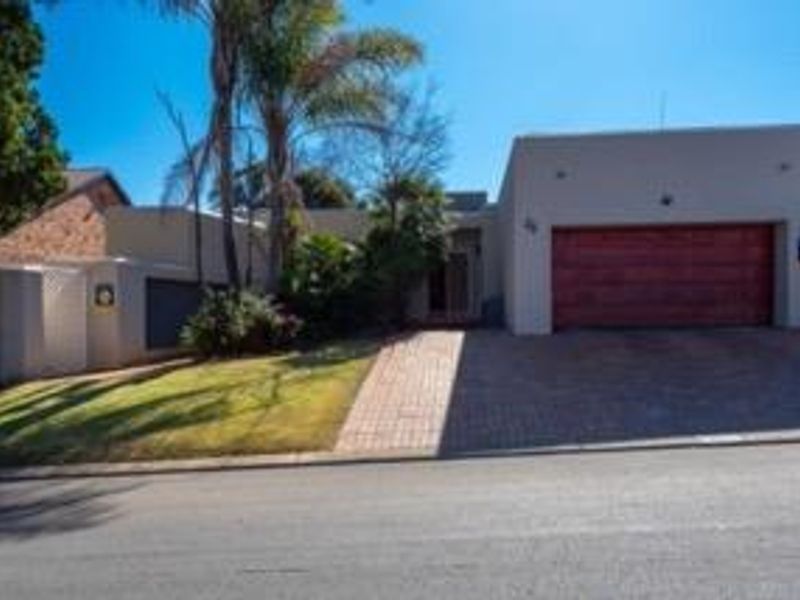 Front elevation of a residential property featuring a paved driveway, double garage, and established garden area.
