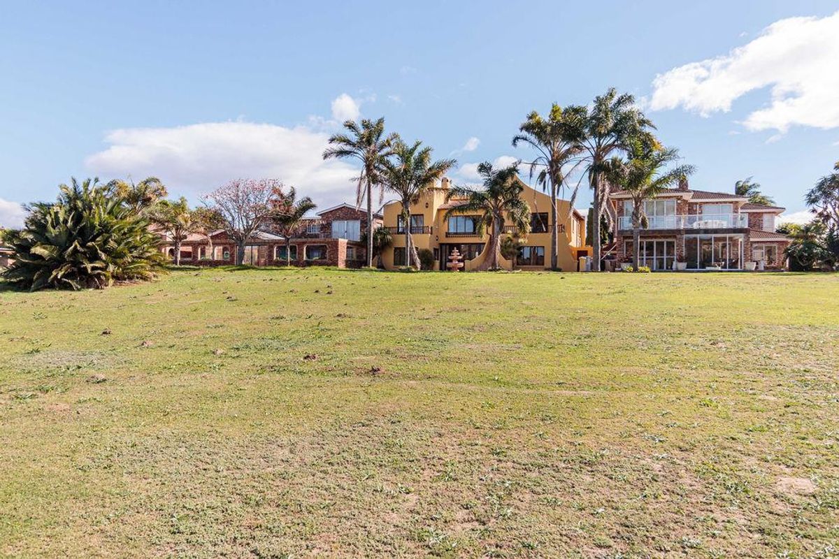 A wide-angle view of the rear elevation of a multi-story residential property featuring expansive lawn space and mature palm trees.