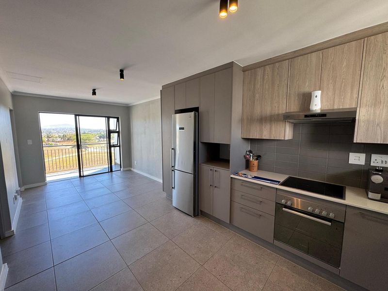 Modern open-plan kitchen and living area featuring sleek cabinetry, integrated appliances, tiled floors, and a sliding door leading to a balcony with scenic views.