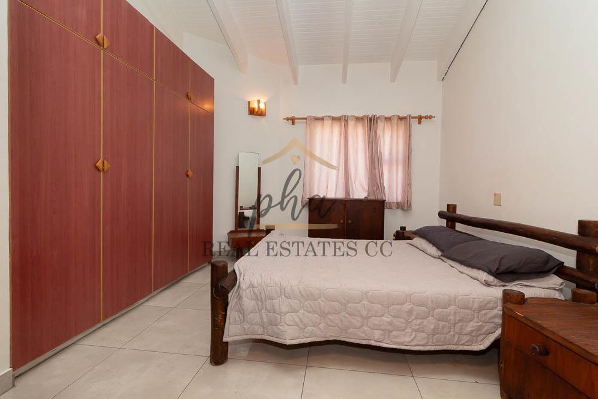 A bedroom featuring built-in floor-to-ceiling wooden wardrobes, tiled flooring, and a vaulted ceiling with exposed beams.