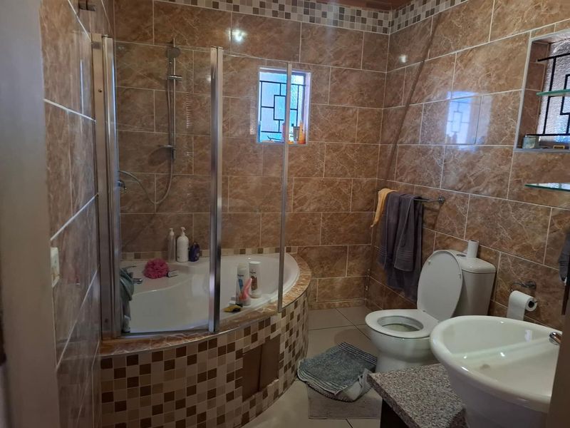 A functional bathroom featuring a corner bathtub with a glass shower enclosure, pedestal basin, and full-height ceramic wall tiling.