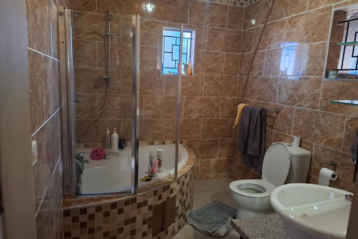A functional bathroom featuring a corner bathtub with a glass shower enclosure, pedestal basin, and full-height ceramic wall tiling.