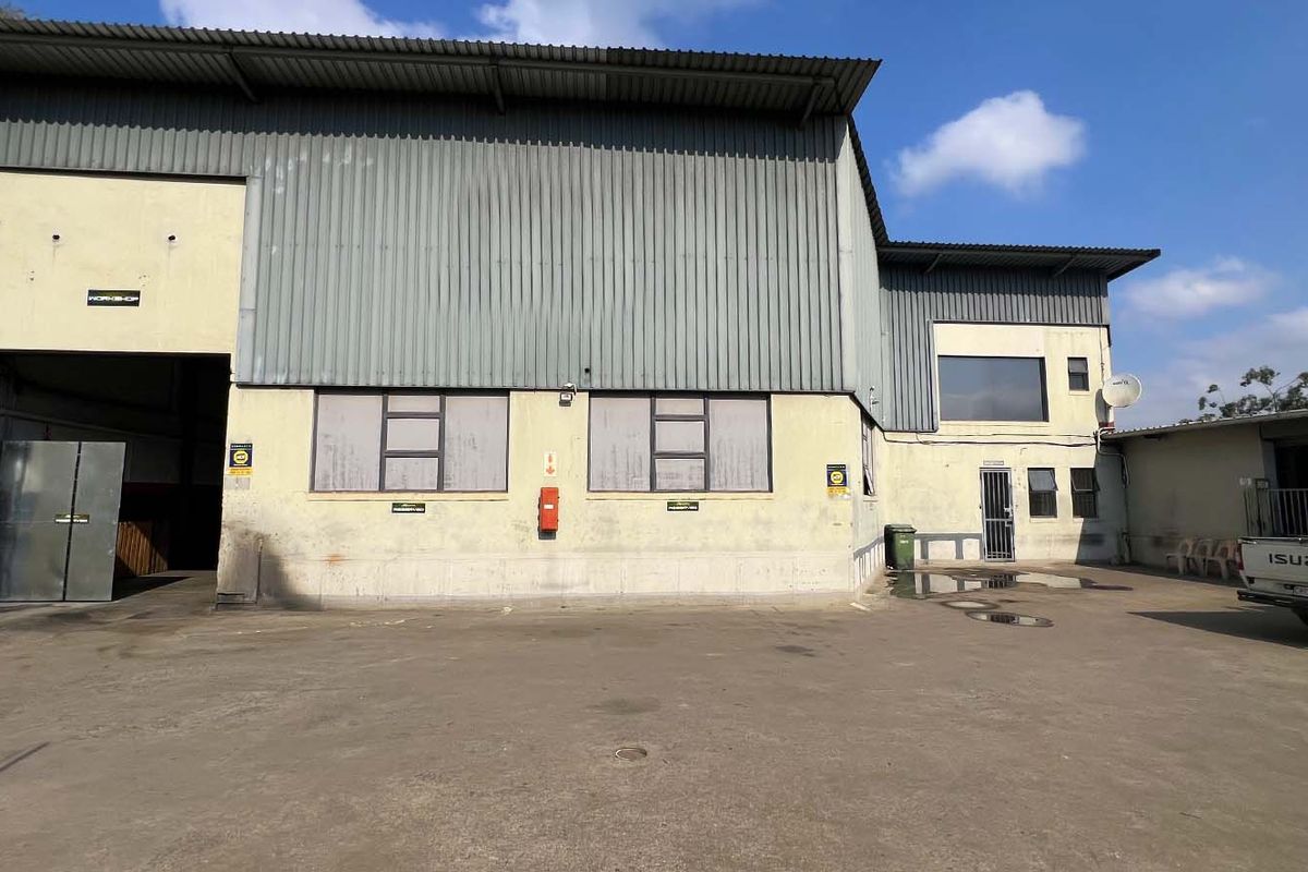 Industrial warehouse exterior featuring corrugated metal cladding, a large roller shutter door, and a paved yard area.