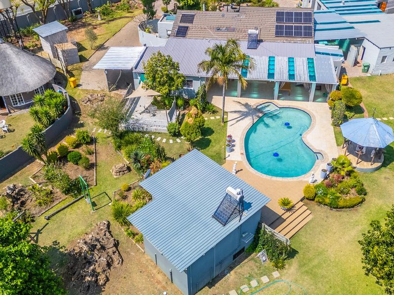 Aerial view of a small holding property featuring a main residence with solar panels, a swimming pool, a gazebo, and extensive landscaped garden areas.