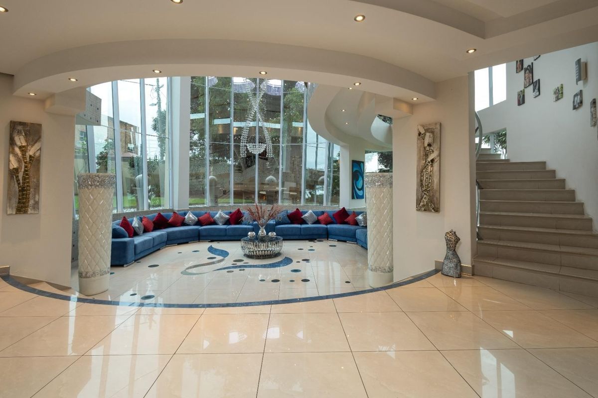 Spacious living area featuring a unique curved architectural ceiling, floor-to-ceiling windows, tiled flooring with decorative inlay, and an integrated staircase.