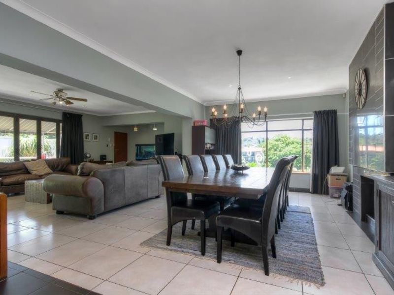 Spacious open-plan living and dining area featuring tiled flooring, a feature fireplace wall, and large windows providing natural light.