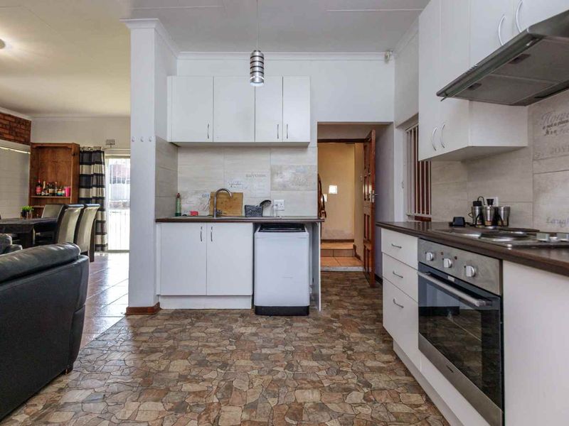 Open plan kitchen featuring white cabinetry, built-in oven, hob, extractor fan, and tiled flooring, seamlessly connecting to the adjacent living and dining area.
