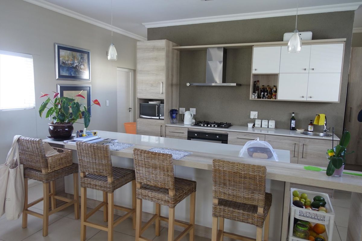 Modern kitchen featuring light wood-tone cabinetry, a gas hob with extractor, built-in oven, and a spacious breakfast bar with tiled flooring.
