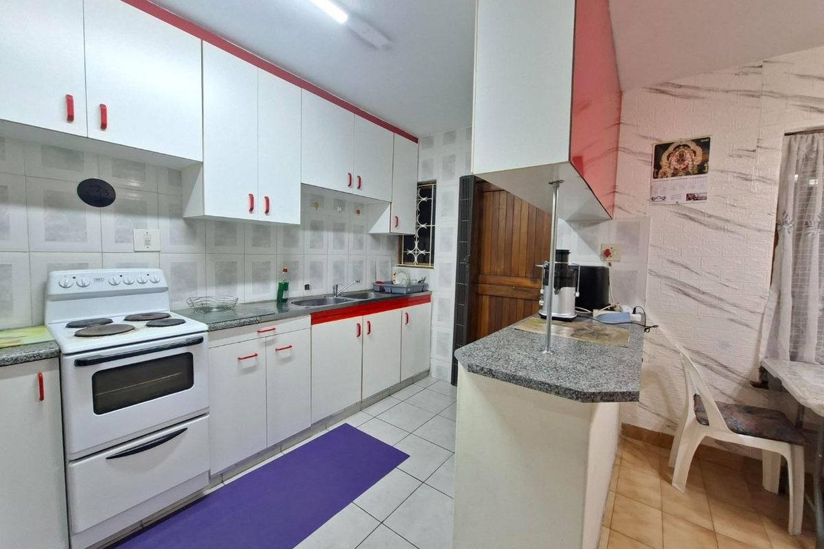 A functional kitchen featuring white cabinetry with red accents, granite countertops, a double basin sink, and a breakfast bar area.