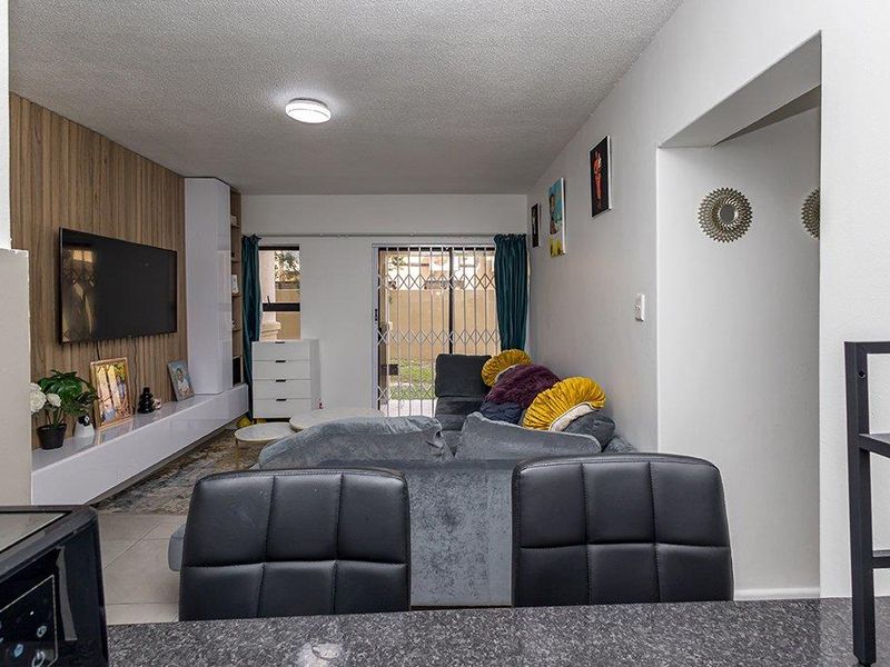 Open-plan living area featuring a modern wood-look media wall, tiled flooring, and a sliding glass door providing access to the exterior.