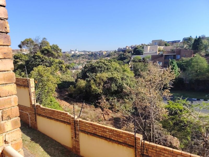 Elevated view overlooking a lush green valley and surrounding residential neighborhood, featuring a brick boundary wall with integrated electric fencing.