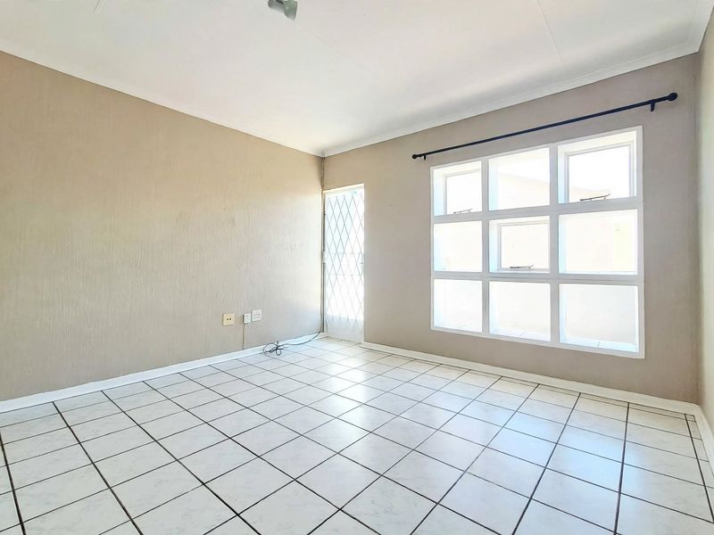A bright, empty living area featuring tiled flooring, a large grid window, and a security gate, offering a clean canvas for personalization.