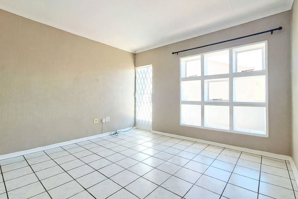 A bright, empty living area featuring tiled flooring, a large grid window, and a security gate, offering a clean canvas for personalization.
